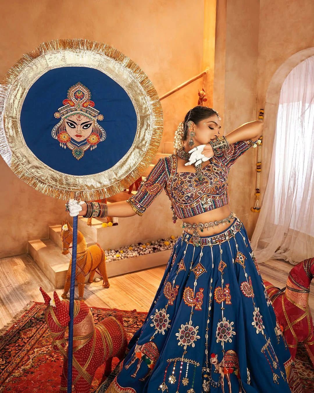 Woman in traditional outfit holding a decorative mirror with an embroidered design.