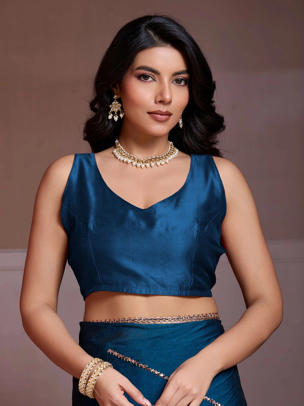 Woman wearing a blue blouse with gold jewelry against a brown background