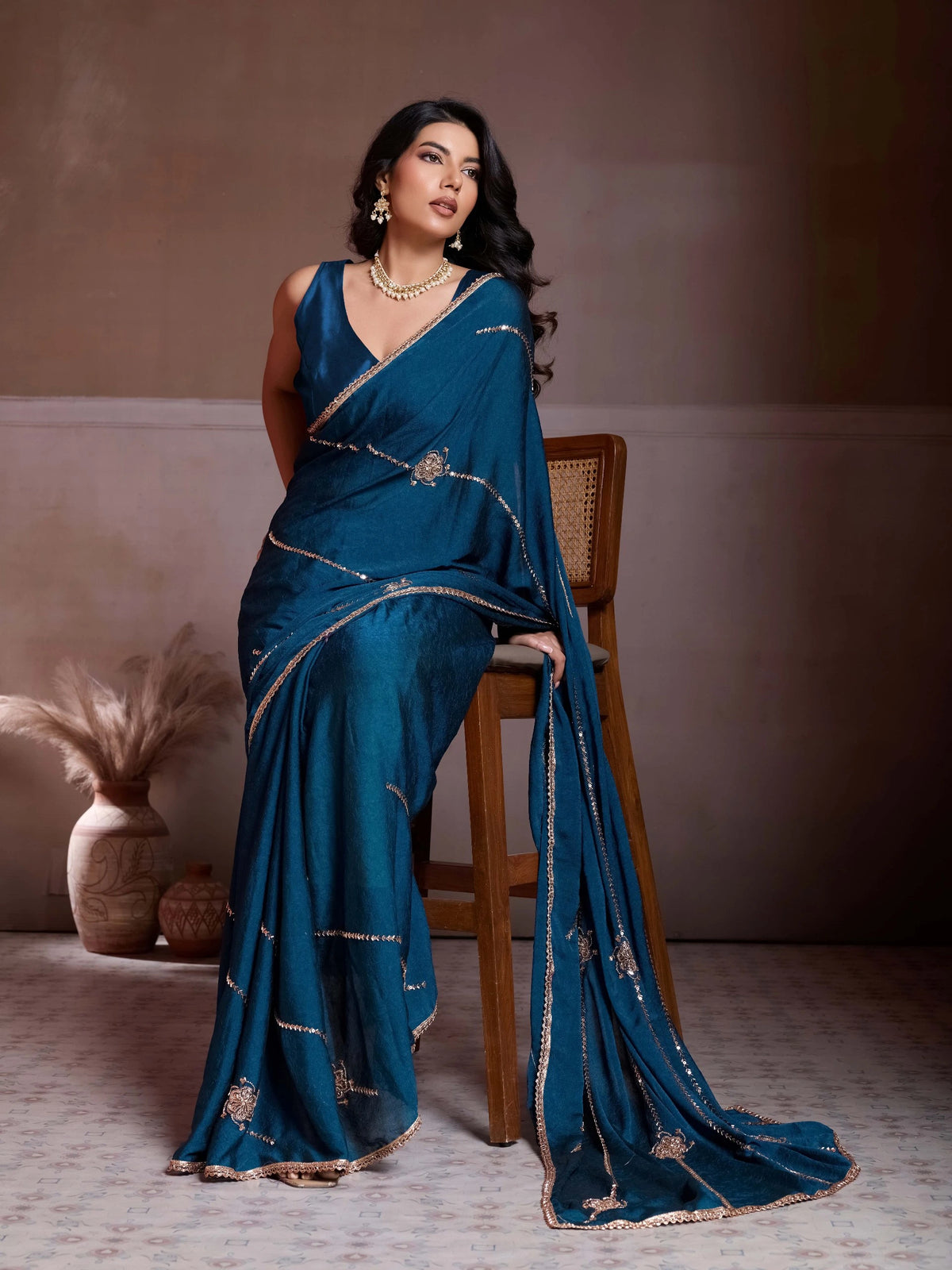 Woman in a blue saree with intricate designs, standing against a neutral background.