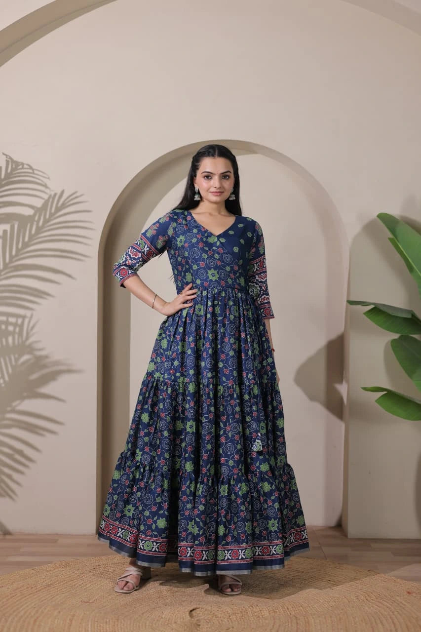 Woman wearing a long, dark blue floral dress standing in front of an archway with plants.