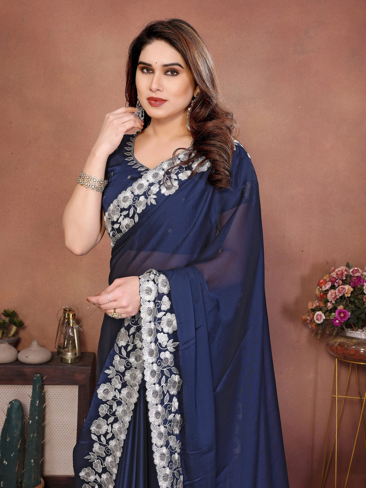 Woman wearing a blue saree with silver floral patterns against a brown background