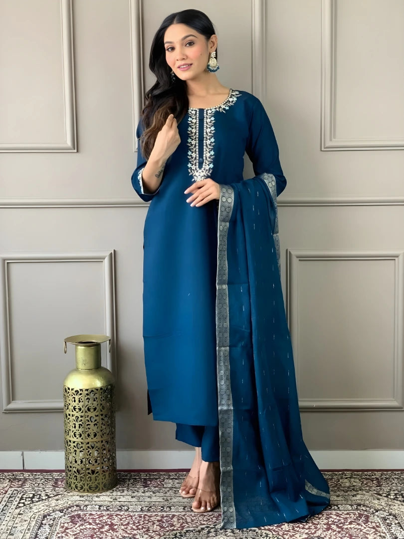 Woman in a blue traditional outfit with a matching dupatta against a neutral wall.