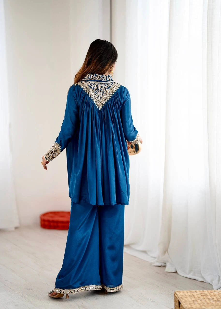Woman wearing a blue outfit with intricate patterns in a room with white curtains.