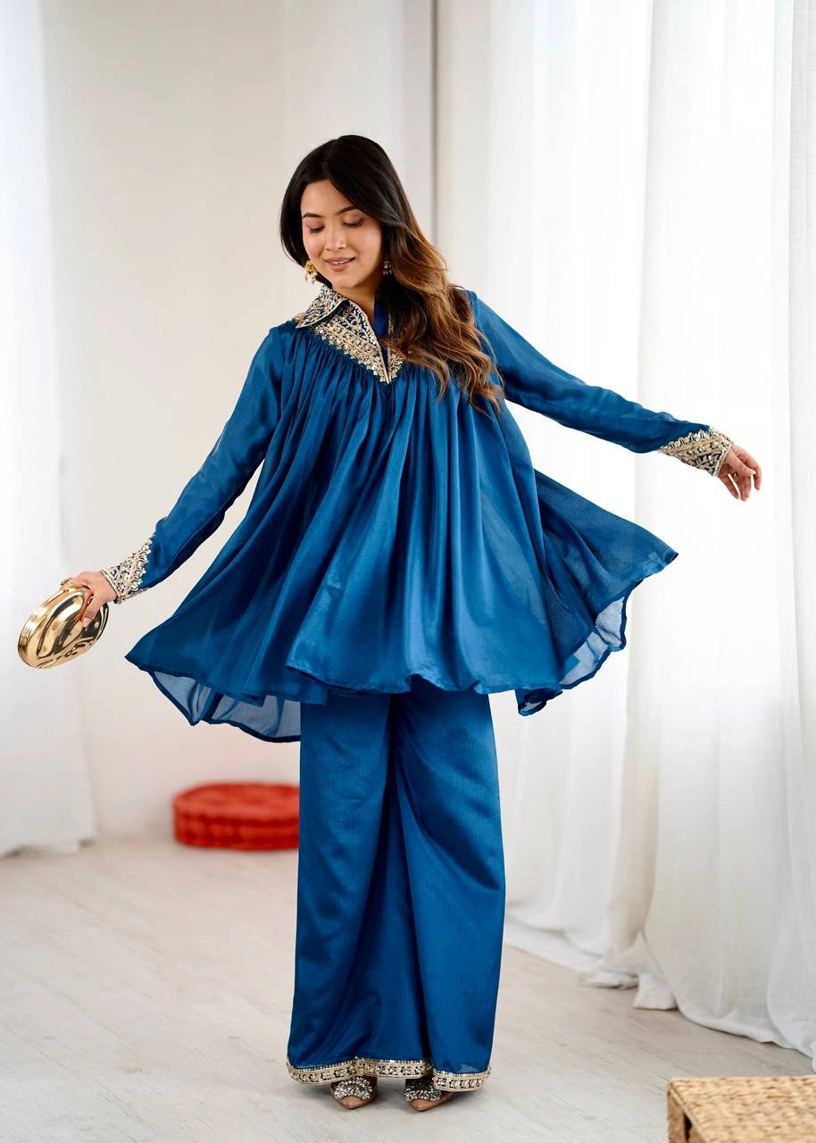 Woman wearing a blue traditional outfit with gold accents in a white room.