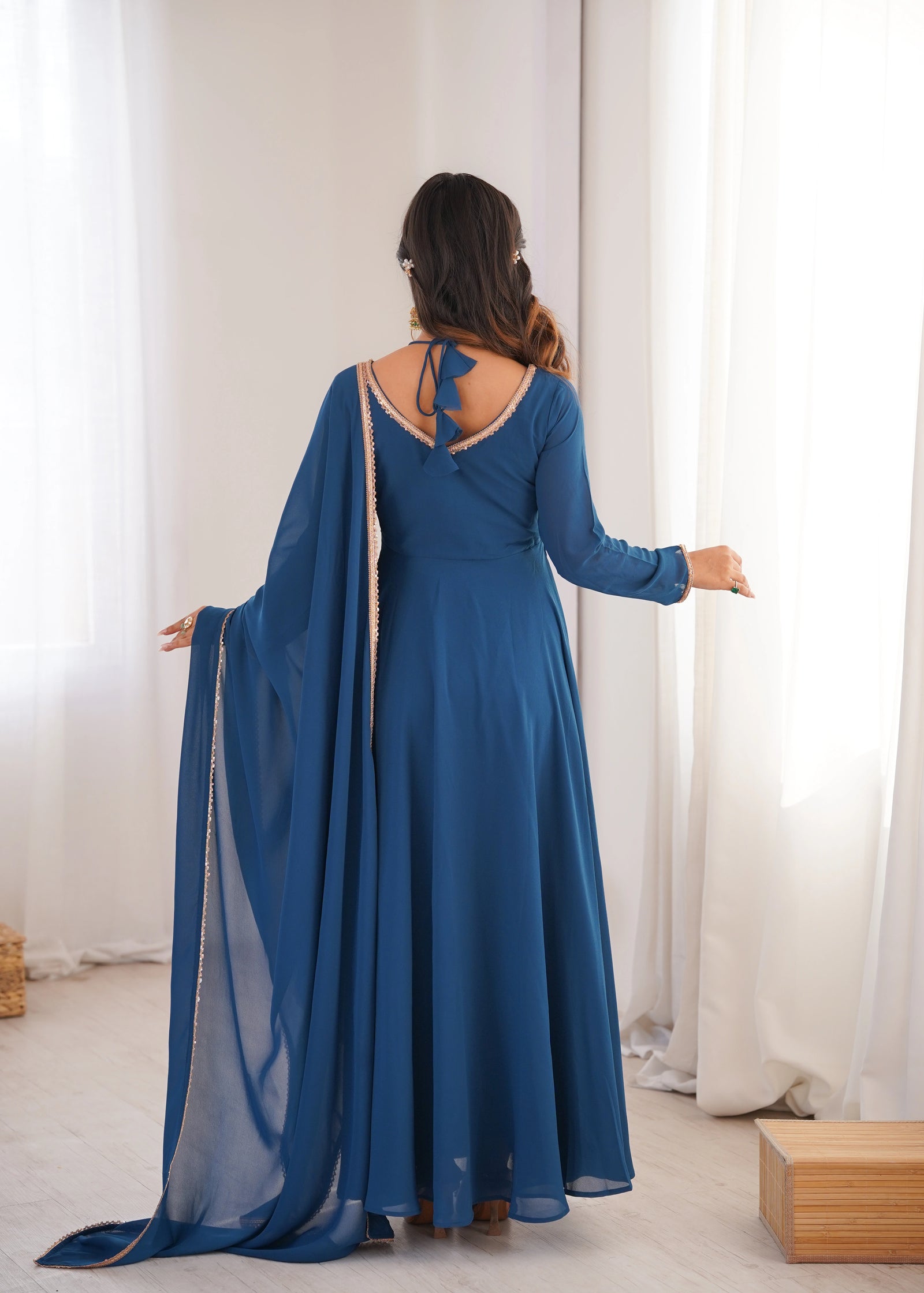 Woman wearing a blue dress with sheer sleeves in a room with white curtains.