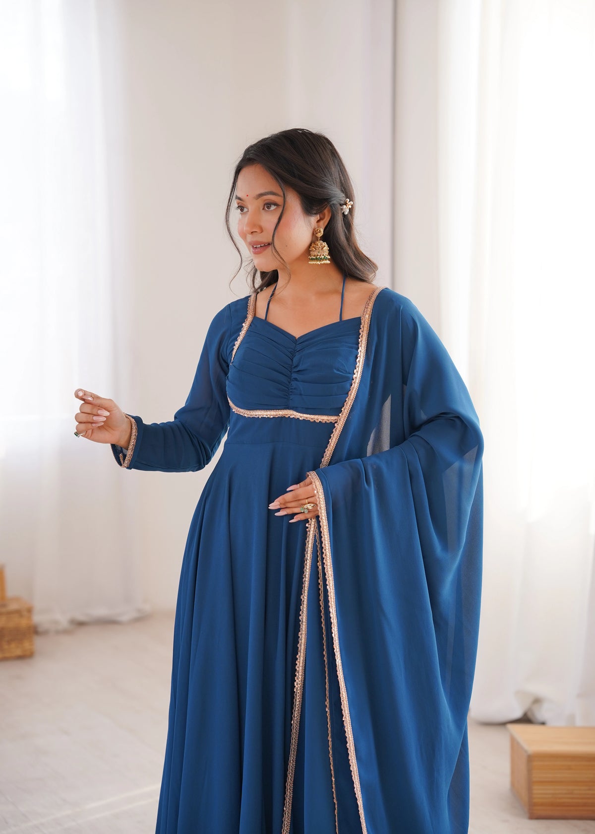 Woman wearing a blue dress with long sleeves and a belt in a bright room.