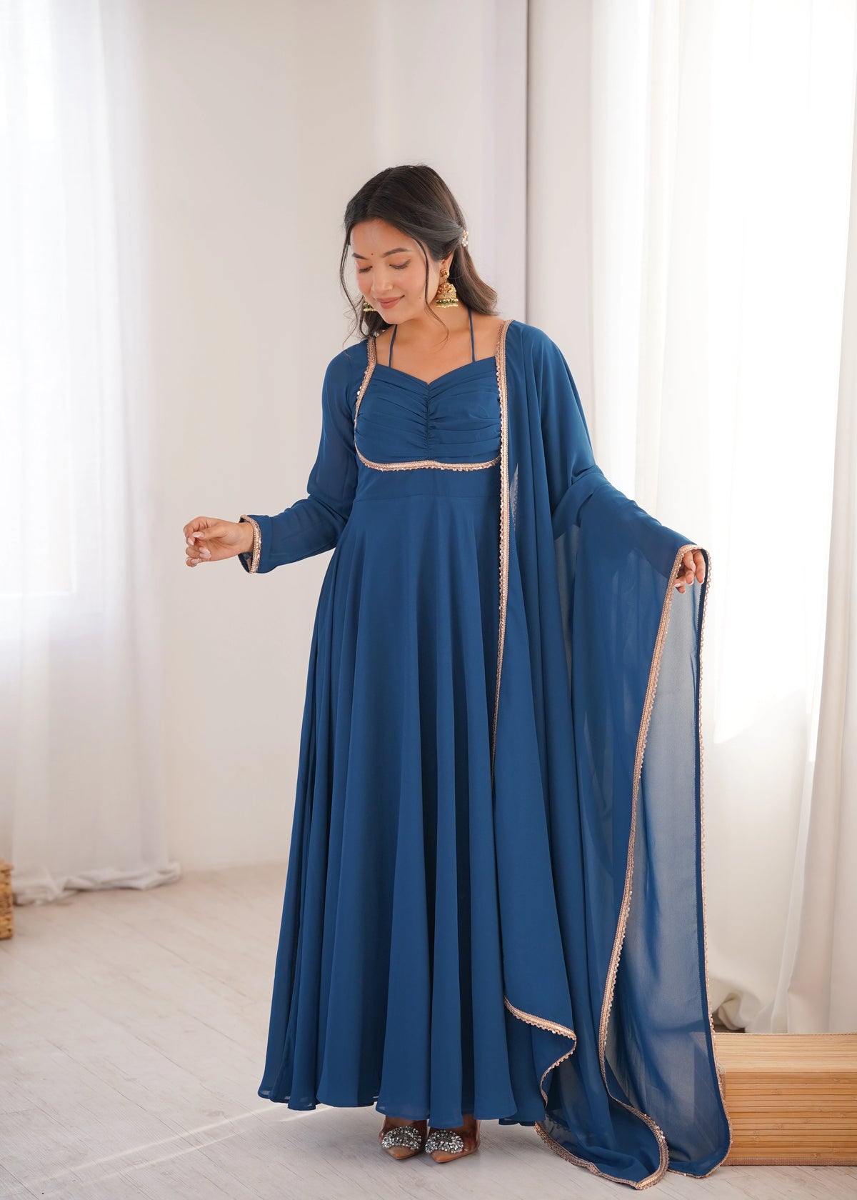 Woman in a blue dress with a long train standing in a room with white curtains.