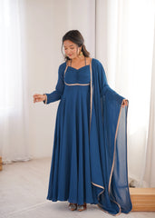Woman in a blue dress with a long train standing in a room with white curtains.