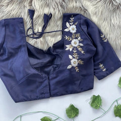 Navy blue blouse with floral embroidery on a white surface with green leaves.