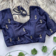 Navy blue blouse with leaf embroidery on a white surface with green leaves.