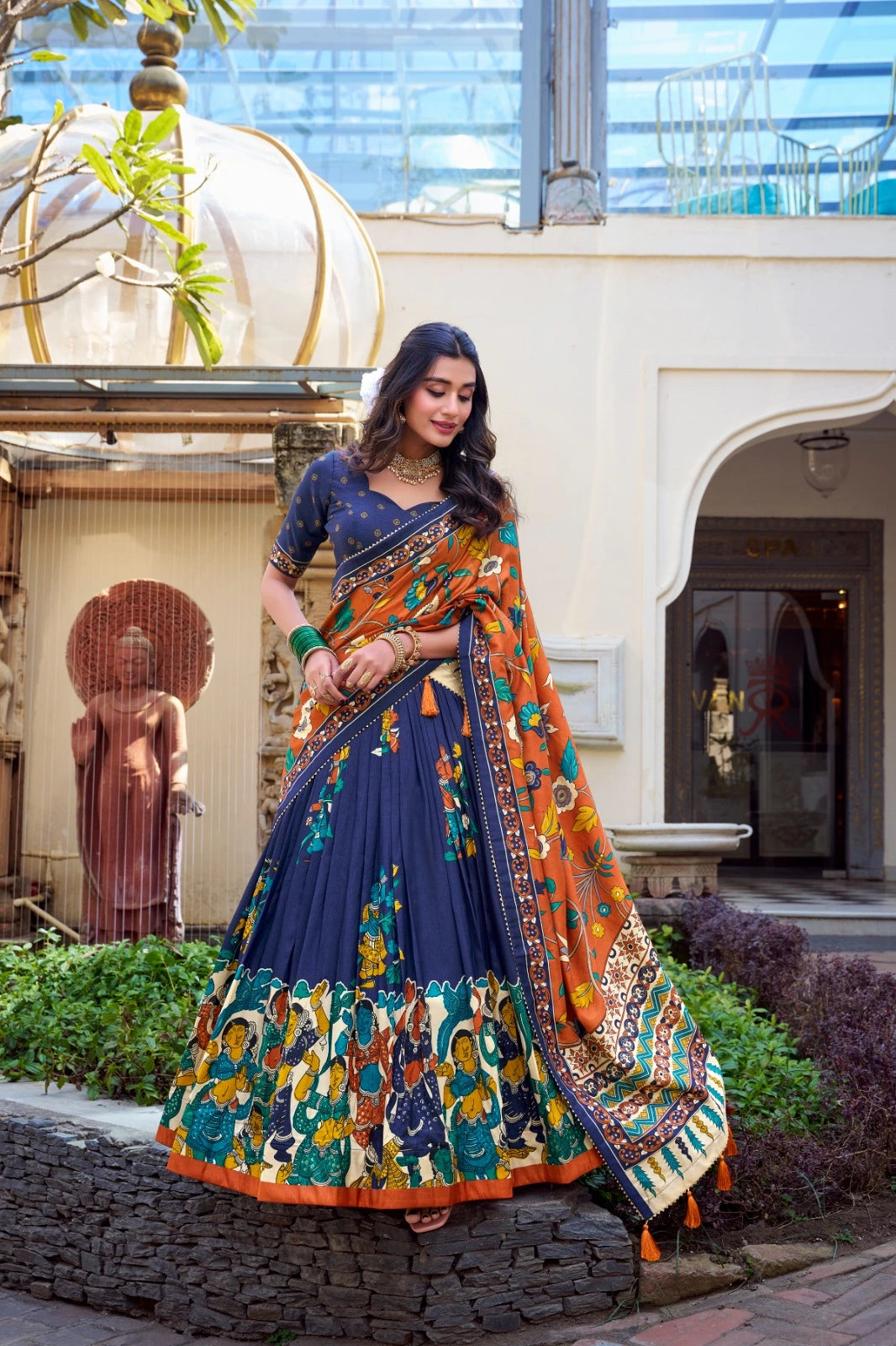Woman in a colorful traditional outfit standing outdoors with architectural elements in the background