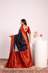 Woman wearing a traditional saree with a red and blue pattern, standing against a plain background.