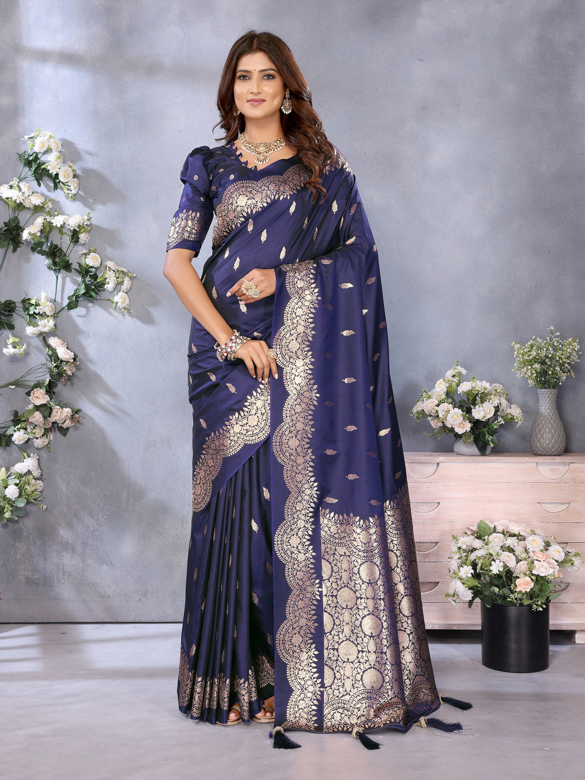 Woman wearing a blue saree with gold embroidery in a decorated room.