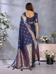 Woman wearing a blue saree with white patterns, standing against a gray wall with floral decorations.