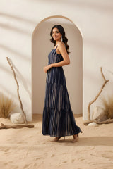 Woman in a long dark blue dress standing in a desert-like setting with archway and minimal decor.