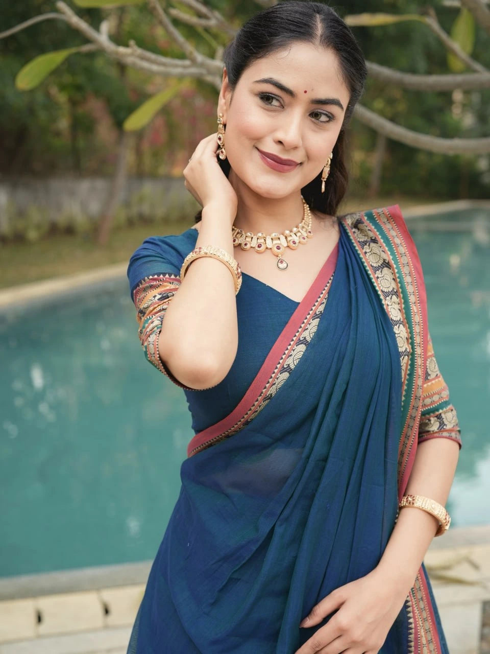 Woman in a blue saree with a pool and greenery in the background