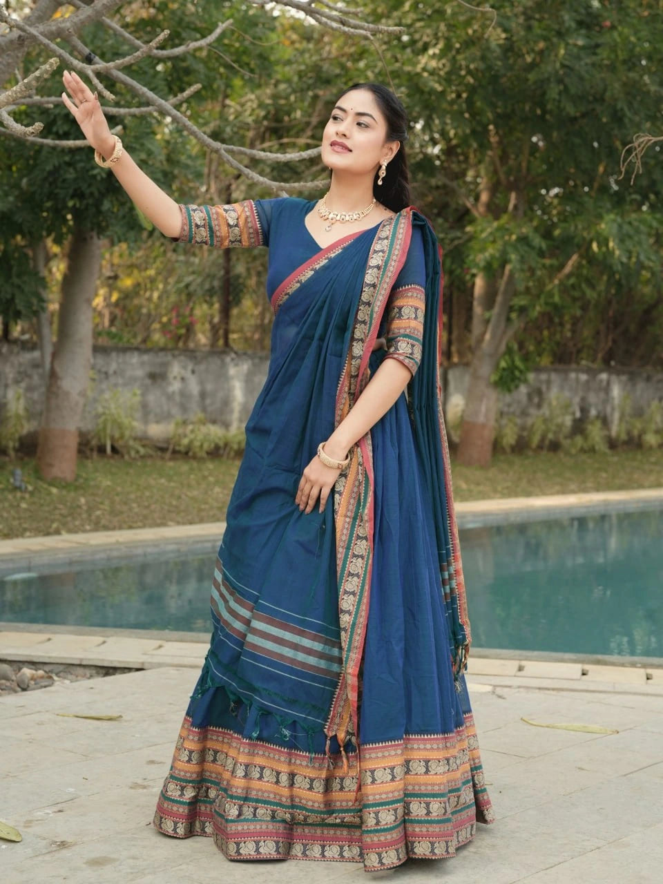 Woman in a blue saree with a patterned border standing by a poolside.