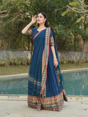 Woman in a blue saree with a patterned border standing by a poolside.