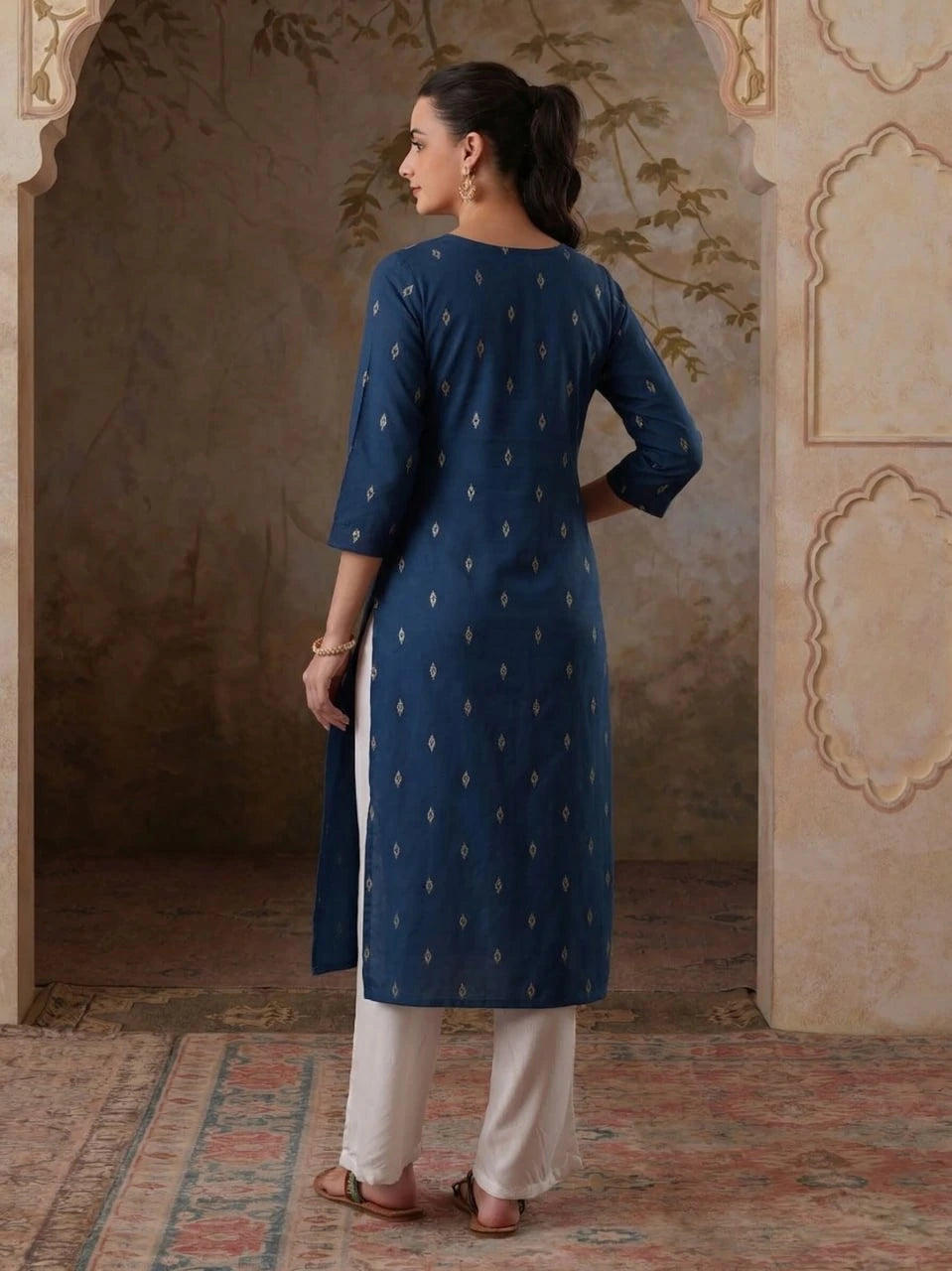 Woman wearing a blue kurta with white pants in an ornate room.
