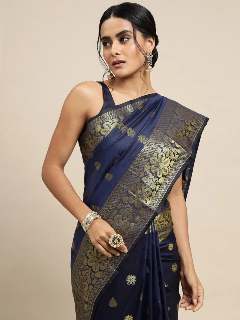 Woman wearing a navy blue saree with gold patterns on a beige background