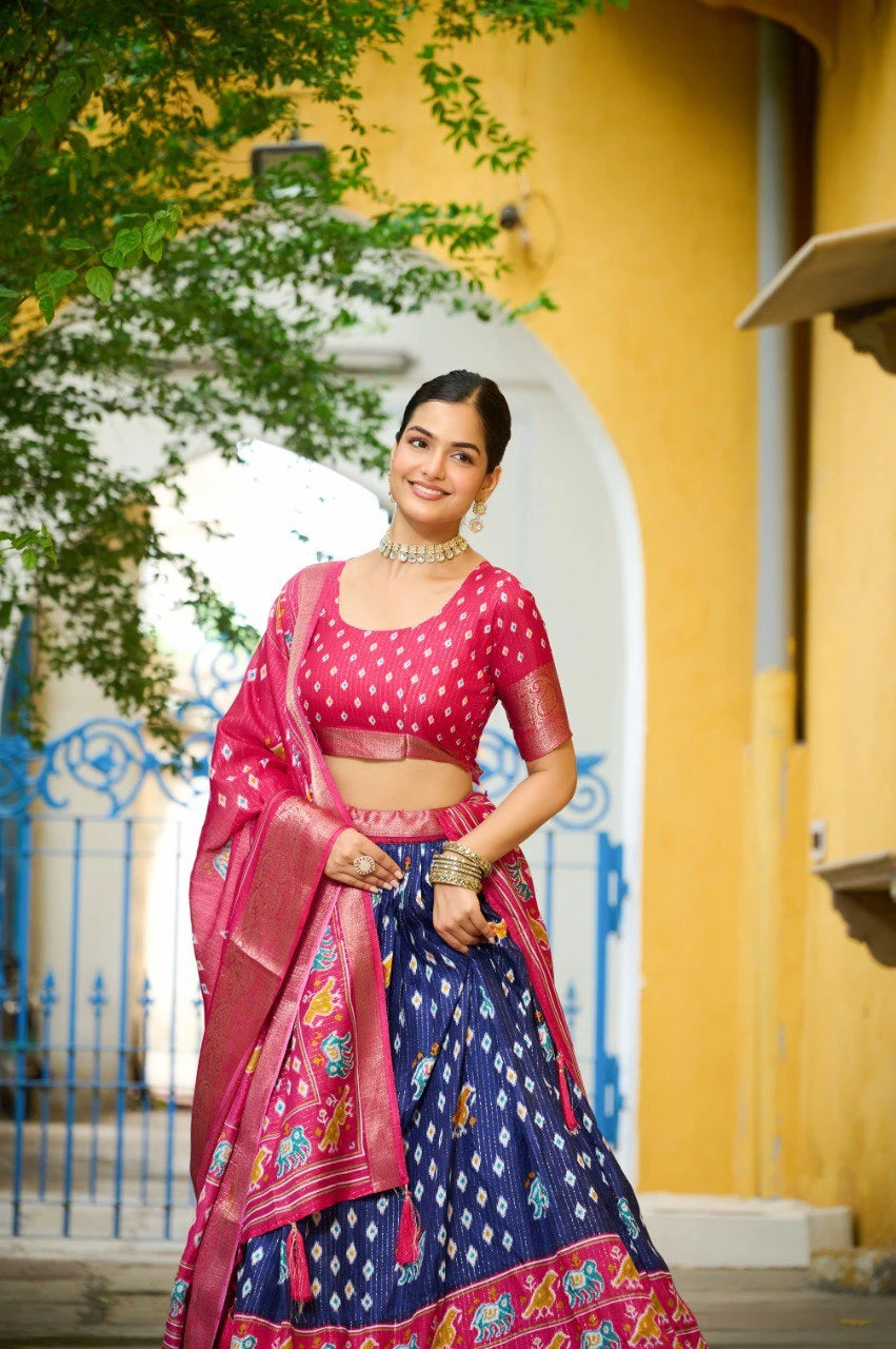Woman in a pink and blue traditional outfit standing in front of a yellow wall with an archway.