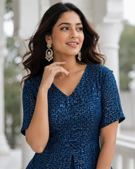 Woman wearing a blue patterned dress with earrings, standing outdoors.