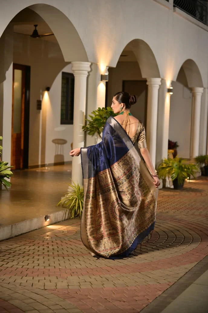 Woman in a traditional saree walking in an outdoor setting with arches and plants.