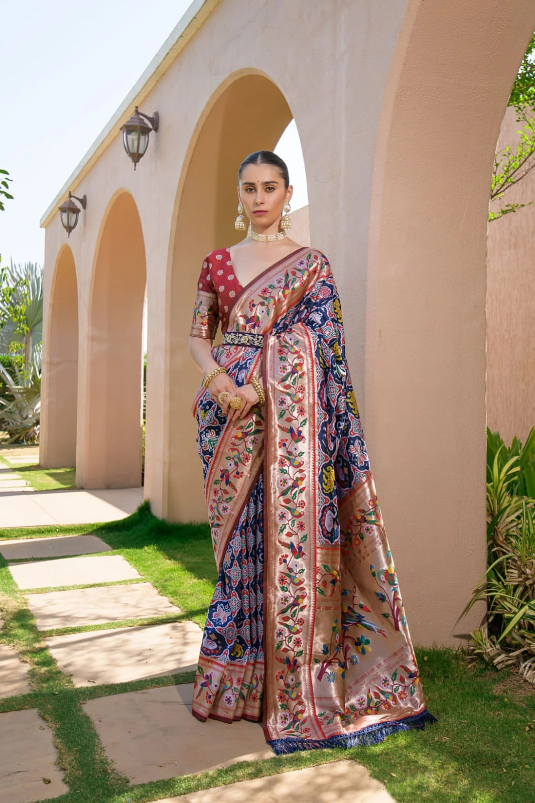 Woman in a colorful saree standing in front of a building with arches.