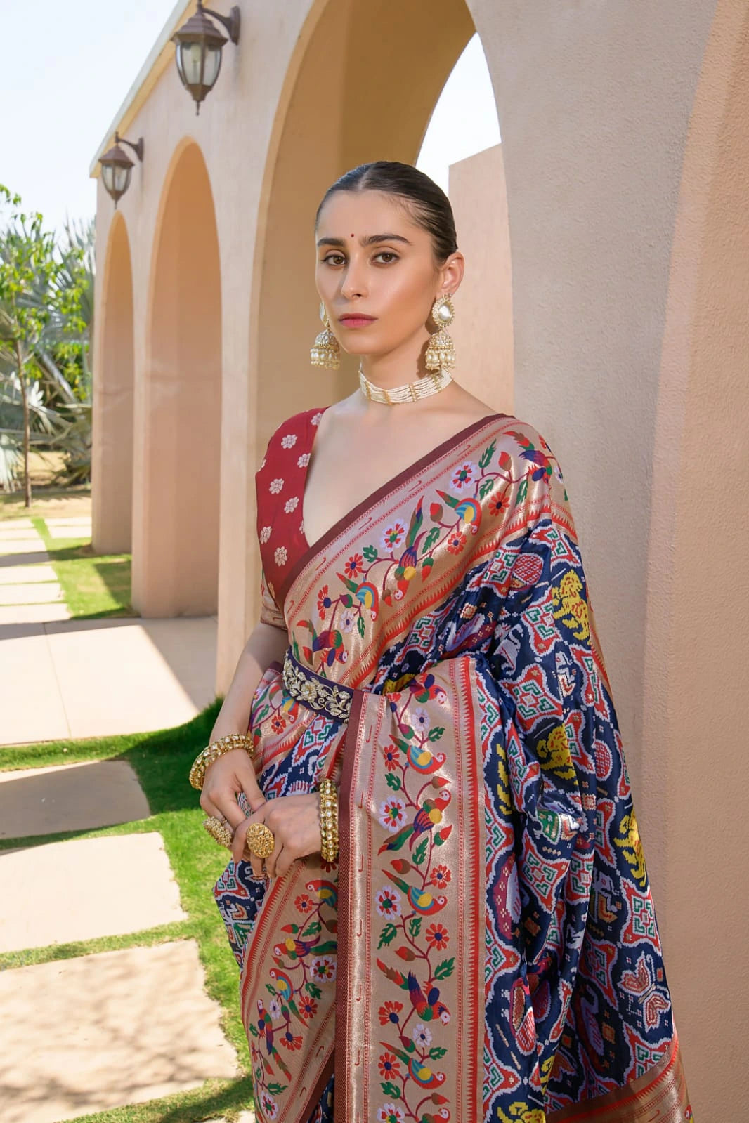 Woman in a colorful saree standing outdoors with architectural elements in the background