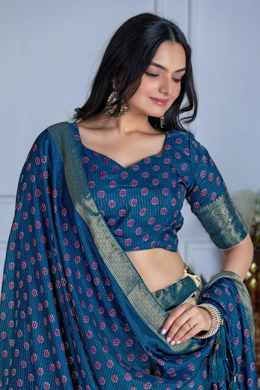 Woman wearing a blue saree with a pattern, standing indoors.