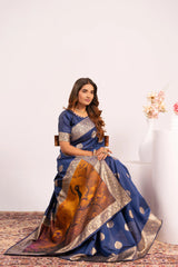 Woman wearing a blue saree with gold patterns sitting on a chair against a white background.