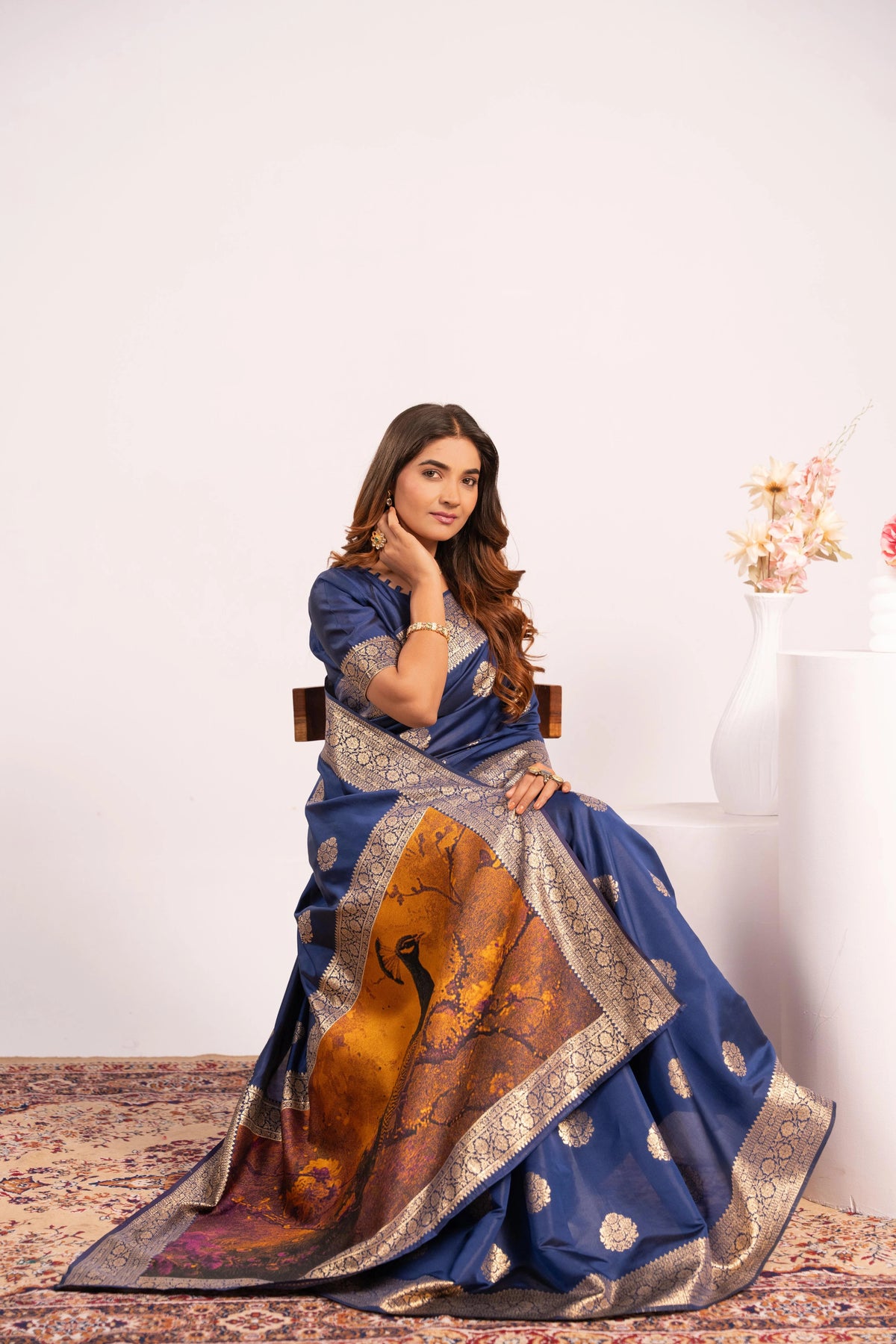 Woman wearing a blue saree with a gold border sitting on a chair.
