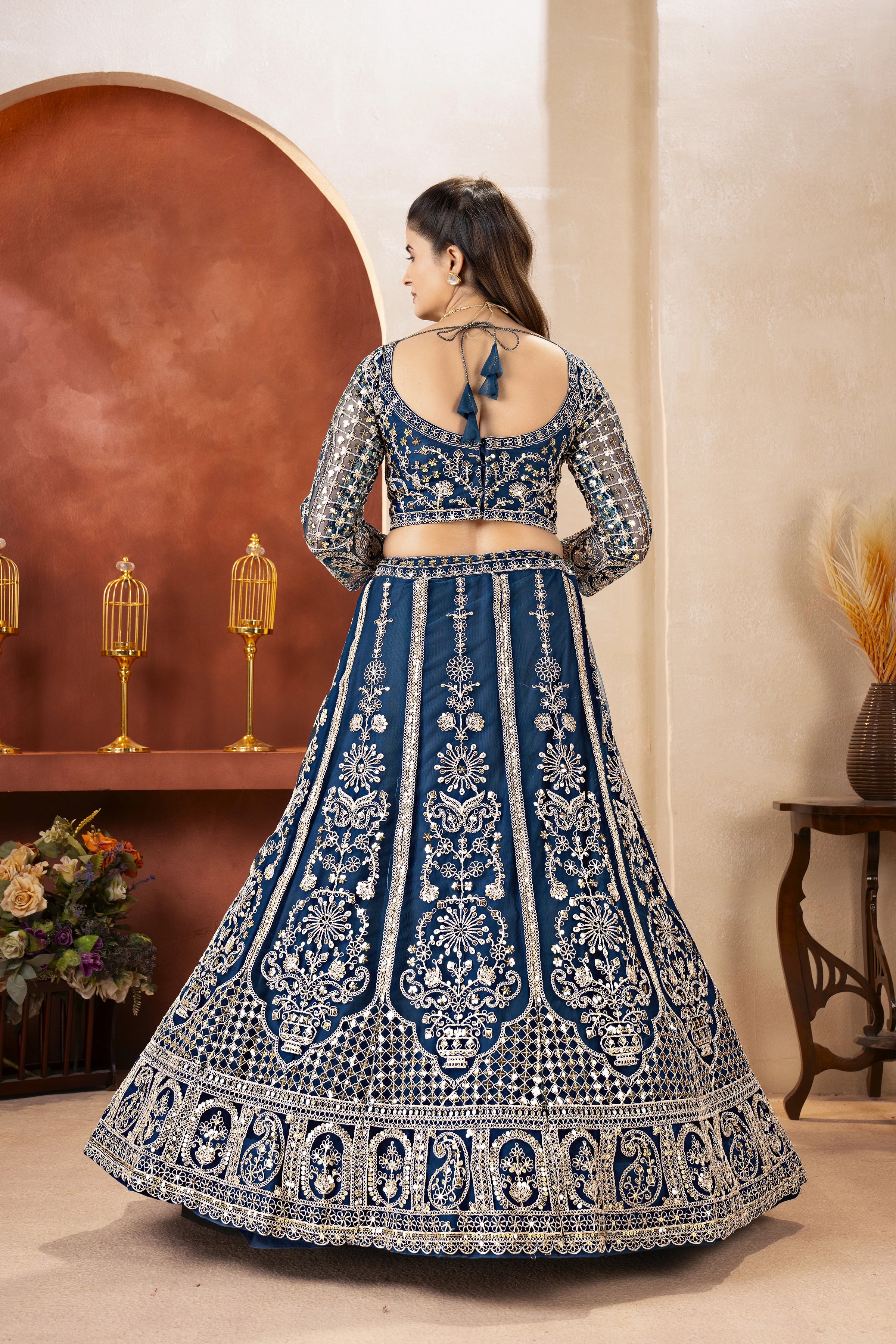 Woman wearing a blue and white embroidered traditional outfit in a decorated room.