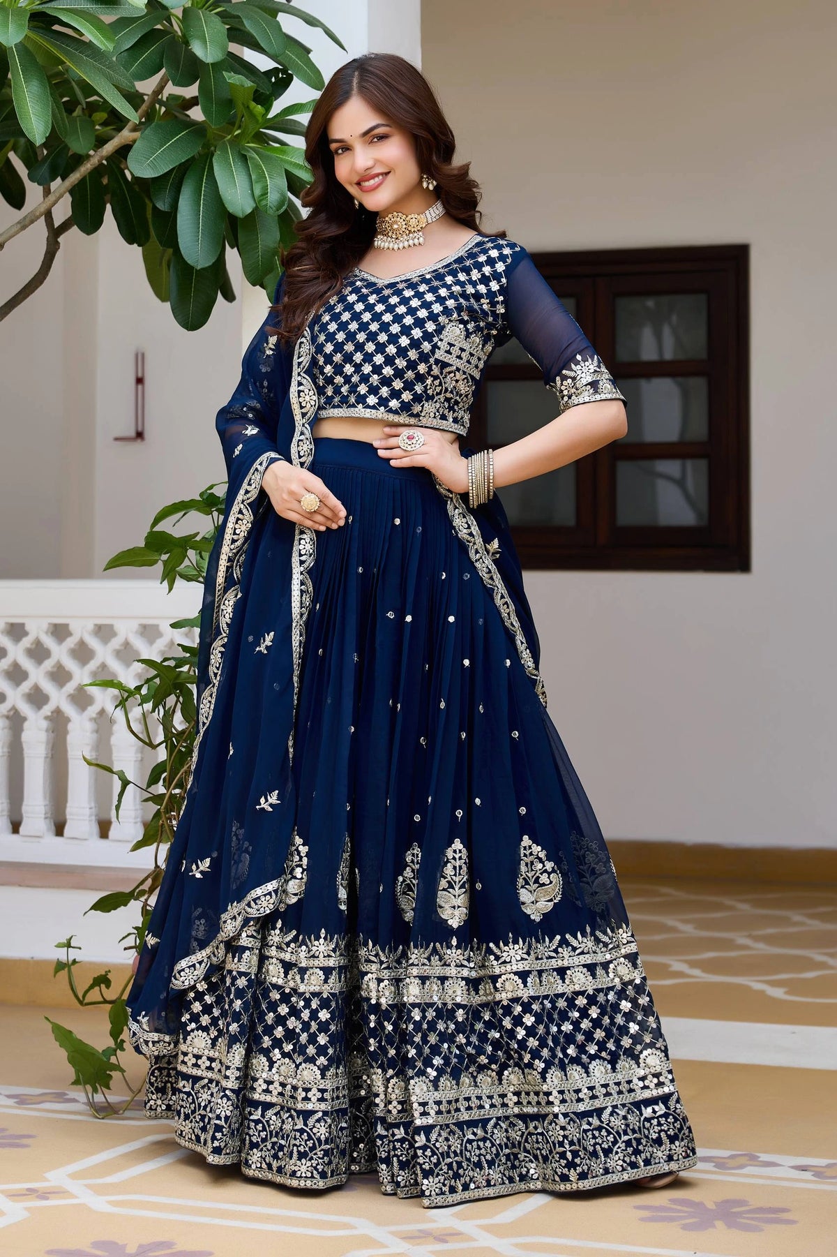 Woman in a traditional navy blue and white outfit with intricate patterns, standing indoors.