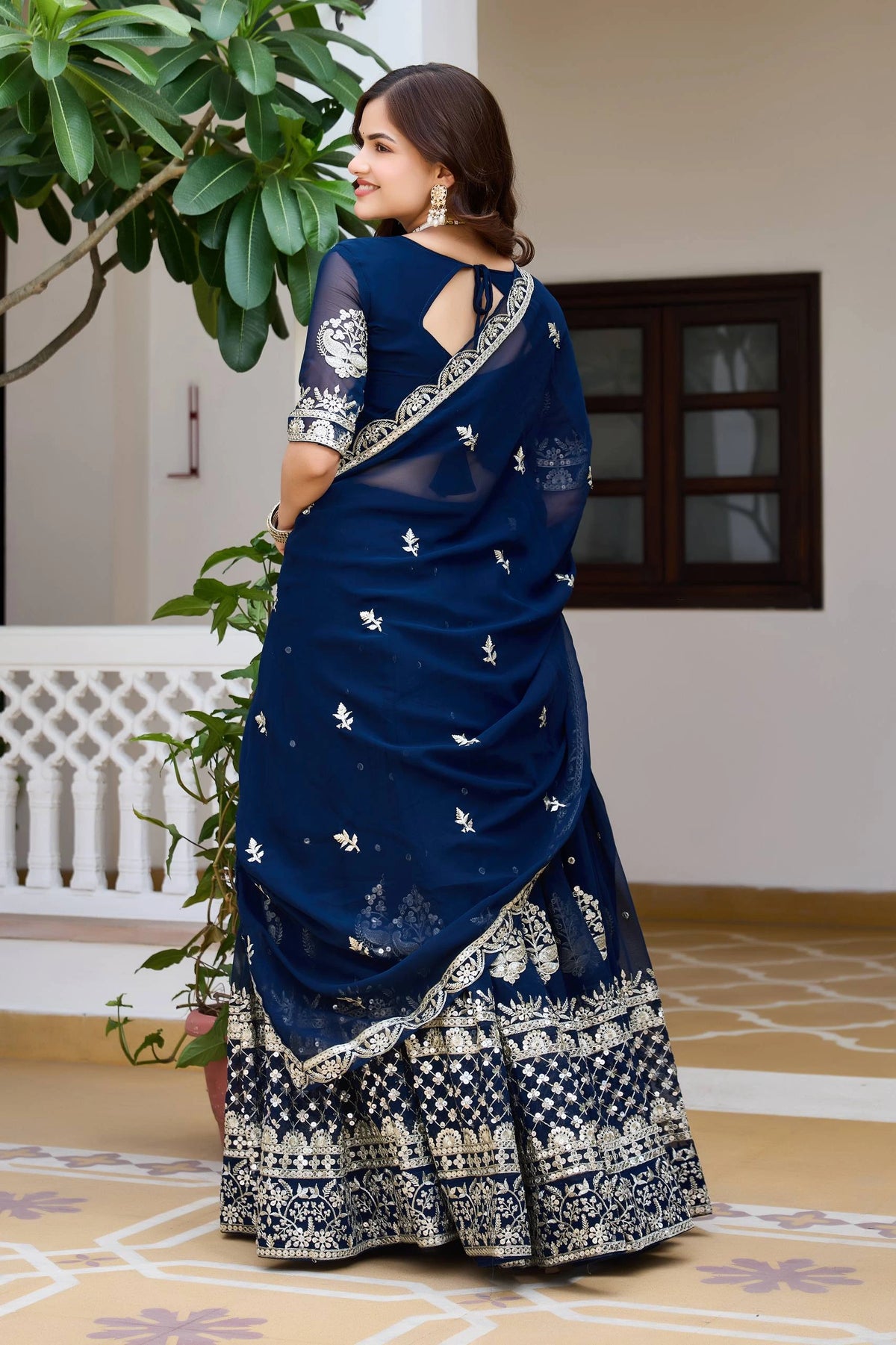 Woman wearing a blue saree with white patterns in an outdoor setting.