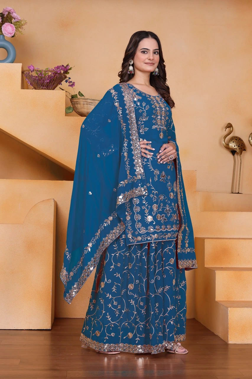 Woman wearing a blue embroidered traditional outfit in a decorated room.