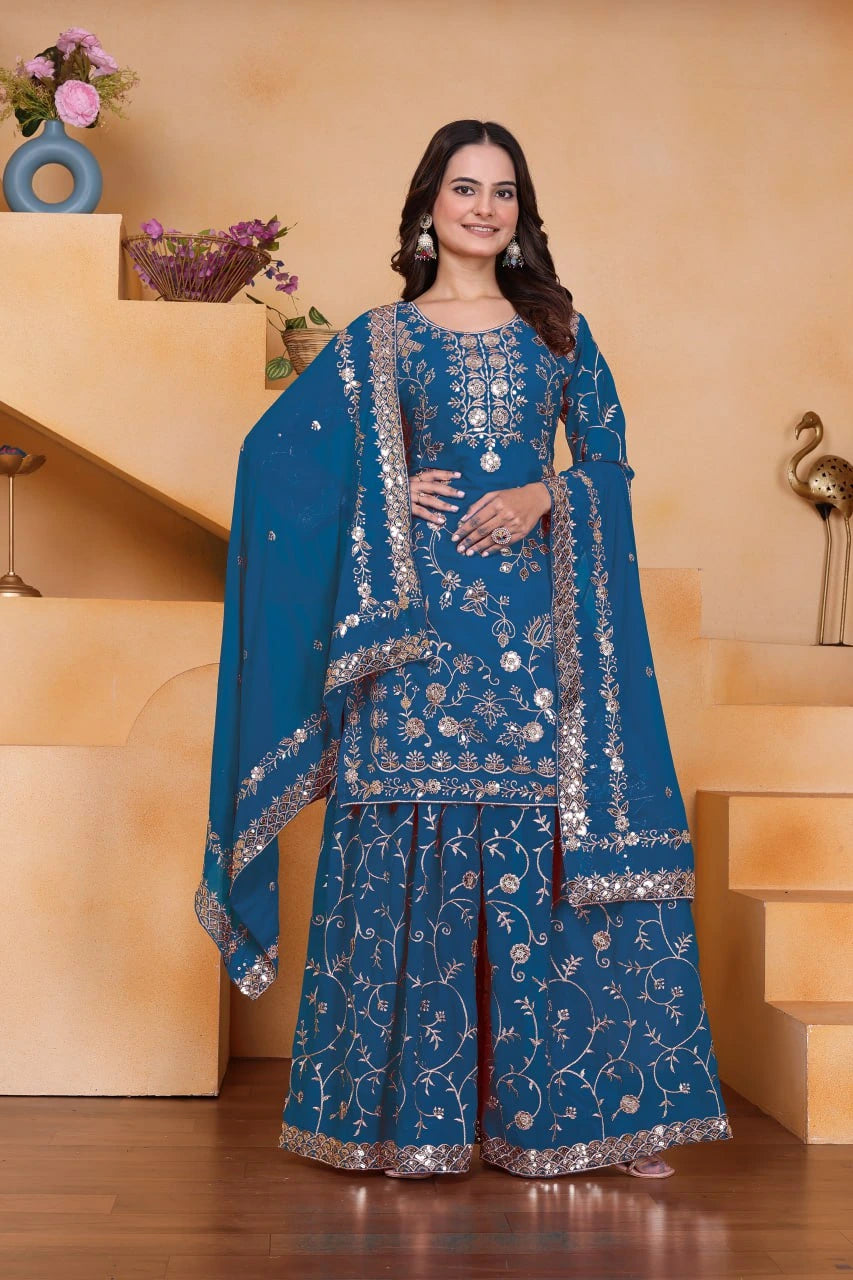 Woman in a blue embroidered traditional outfit standing indoors with a neutral background