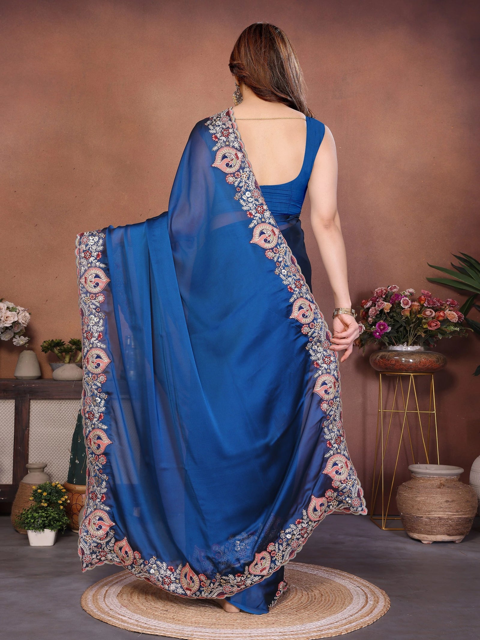 Woman wearing a blue saree with floral patterns in a decorated room.