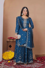 Woman in a blue embroidered traditional outfit standing in a decorated room with flowers and a basket.