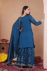 Woman in a blue traditional outfit standing in a decorated room with flowers.