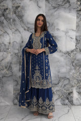 Woman wearing a blue embroidered traditional outfit against a marble wall.
