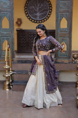 Woman in a traditional outfit with a purple top and white skirt in an ornate room.