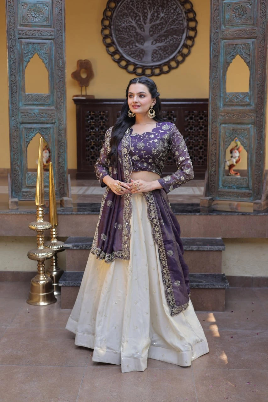 Woman in a traditional outfit standing in a decorated room with ornate wall designs and a tree of life symbol.