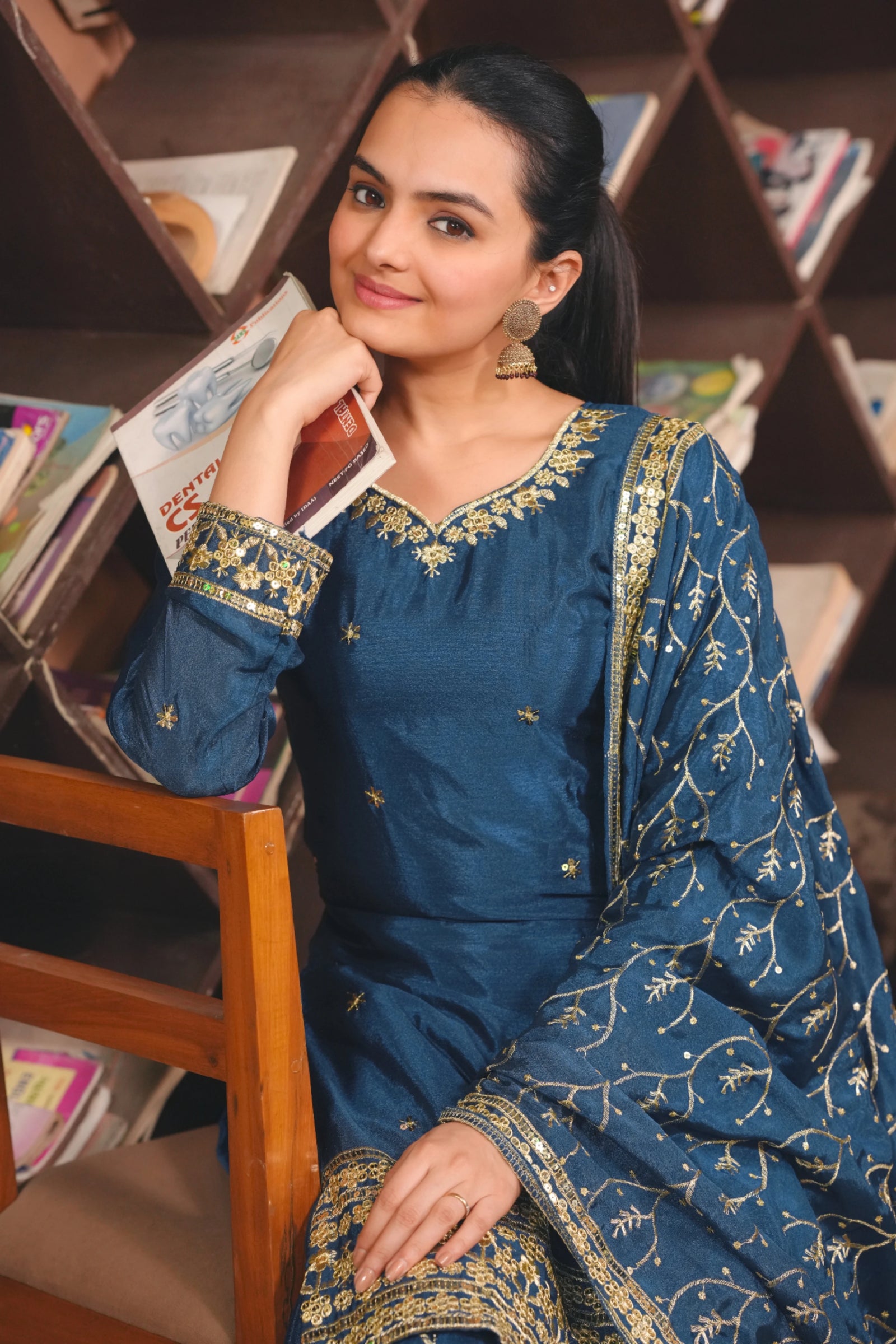 Woman in a blue traditional outfit sitting in front of a bookshelf.