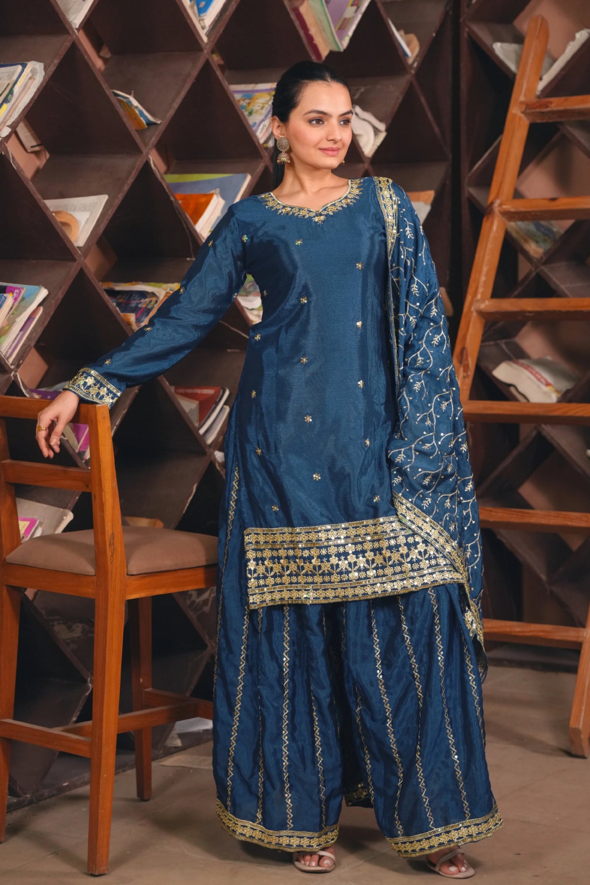 Woman in a blue traditional outfit standing in front of a bookshelf.