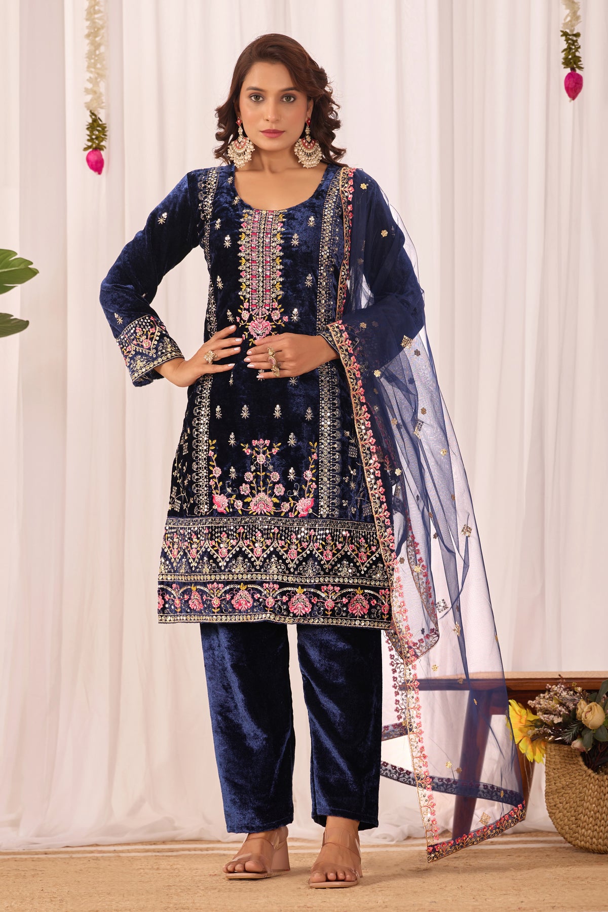 Woman wearing a navy blue embroidered traditional outfit with a white curtain background