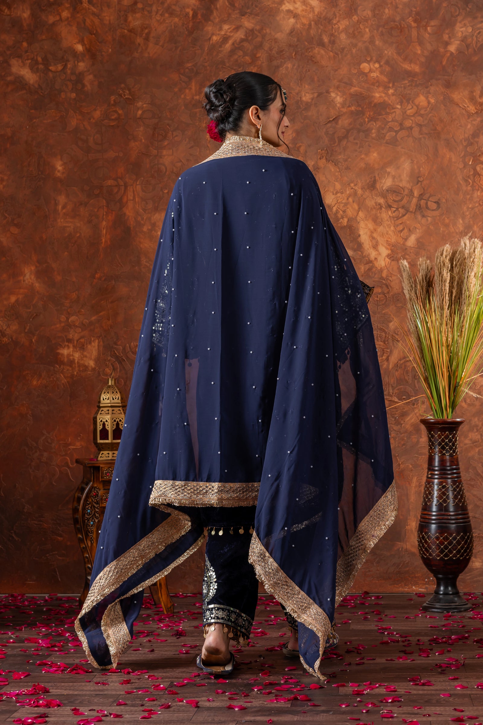 Woman wearing a navy blue embroidered dupatta with gold trim against a brown textured wall.