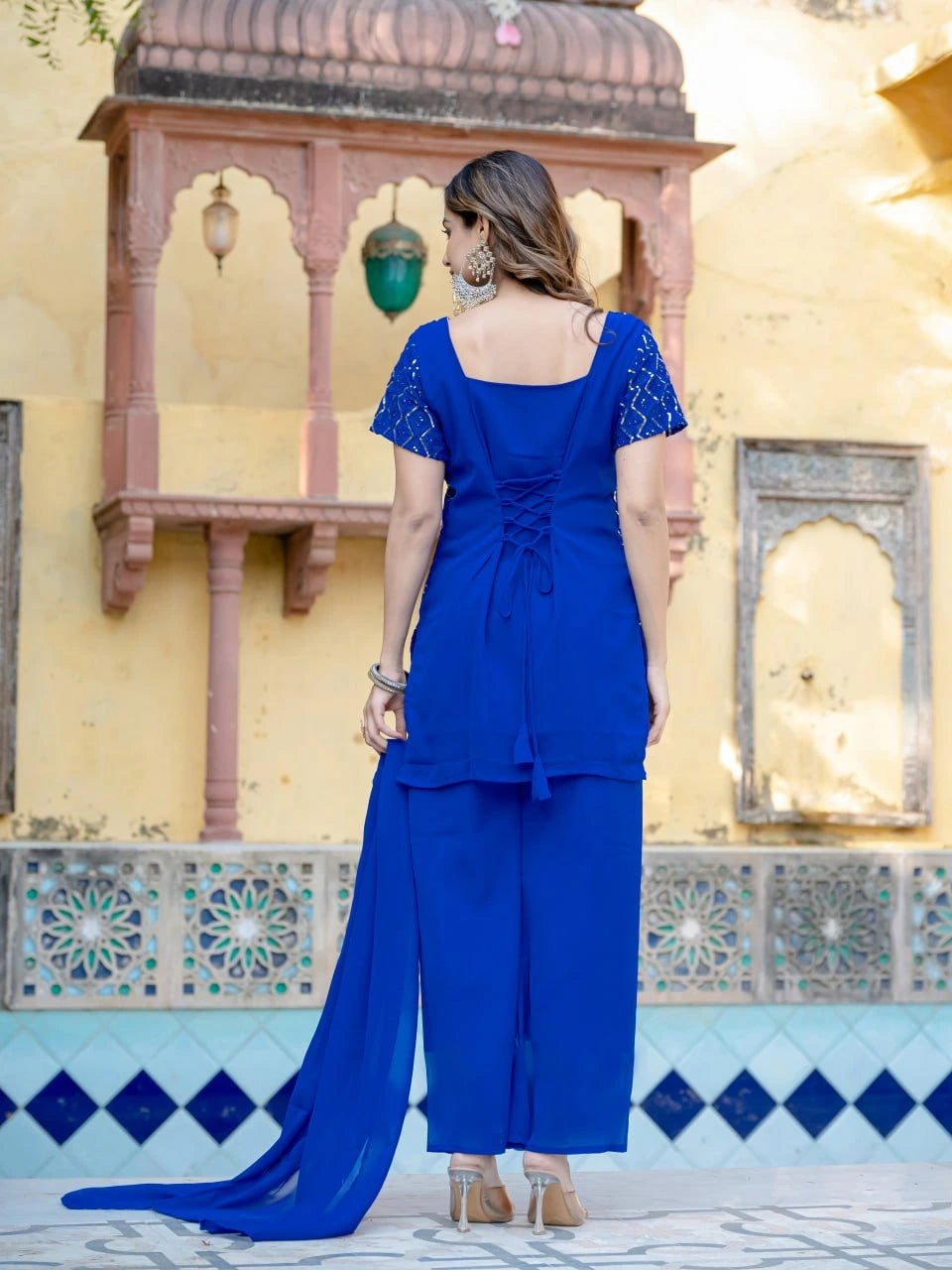 Woman in a blue traditional outfit standing in front of a decorative wall.