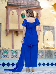 Woman in a blue traditional outfit standing in front of a decorative wall.