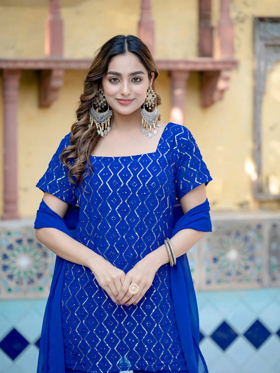 Woman wearing a blue traditional outfit with intricate patterns in an outdoor setting.